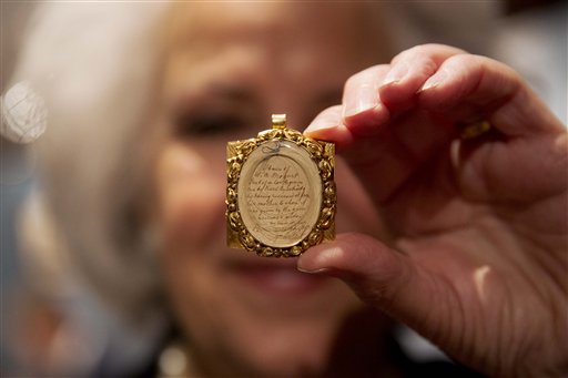 La asistente de galería Sandra Handley posa para fotógrafos con un mechón de pelo de Wolfgang Amadeus Mozart, contenido en un relicario dorado del siglo XIX, el martes 26 de mayo del 2015 en la casa de subastas Sotheby's en Londres. (Foto AP)