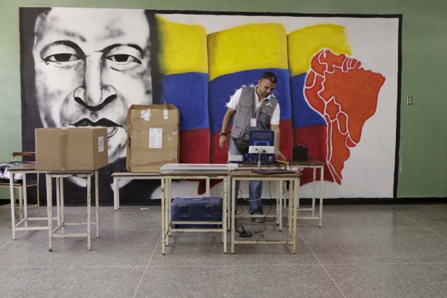 A worker of the National Electoral Council (CNE) configures a voting machine in front of a mural depicting Venezuela's late President Hugo Chavez at a school in Caracas, December 4, 2015. Venezuela will hold parliamentary elections on December 6. REUTERS/Marco Bello FOR EDITORIAL USE ONLY. NO RESALES. NO ARCHIVE.