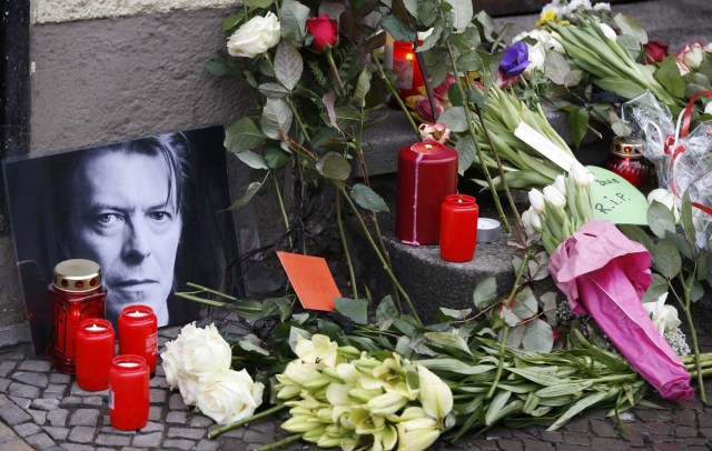 Flowers and lit candles are pictured next to a portrait of David Bowie outside the apartment house where he was living in 1976-78 in Berlin's Schoeneberg district, Germany, January 11, 2016. David Bowie, a music legend who used daringly androgynous displays of sexuality and glittering costumes to frame legendary rock hits "Ziggy Stardust" and "Space Oddity", has died of cancer aged 69.    REUTERS/Fabrizio Bensch
