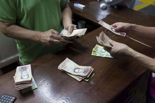 Men count Venezuelan bolivar notes, which they received for their work as carwashers during the week, at a parking lot in Caracas January 22, 2016. REUTERS/Marco Bello