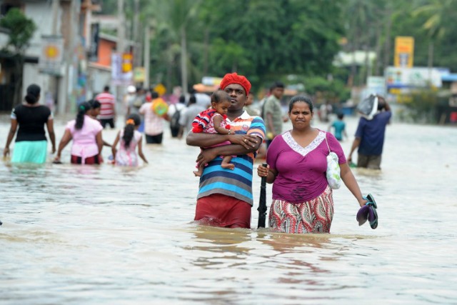 Un par de Sri Lanka con su hijo a hacer su camino a través de las aguas en la zona residencial de Kaduwela en la capital Colombo el 17 de mayo de 2016. Los trabajadores de emergencia en Sri Lanka el 17 de mayo encontraron los cuerpos de una mujer y dos niños que murieron en un deslizamiento de tierra, teniendo el peaje de dos días de fuertes lluvias a 11, con miles más vieron obligados a abandonar sus hogares. LAKRUWAN WANNIARACHCHI / AFP
