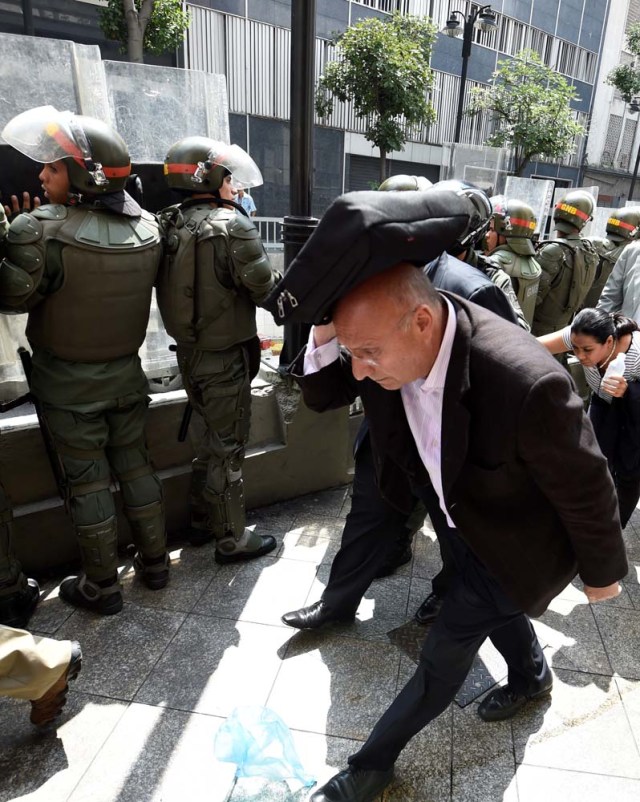 Opposition lawmakers protect themselves while they try to reach the National Assembly in Caracas on October 27, 2016. "We are going to notify Nicolas Maduro that the Venezuelan people declare he has abandoned his post," the speaker of the National Assembly, Henry Ramos Allup, said to cheers from hordes of protesters in Caracas. / AFP PHOTO / JUAN BARRETO