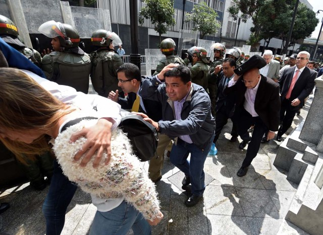 Opposition lawmakers protect themselves while they try to reach the National Assembly in Caracas on October 27, 2016. "We are going to notify Nicolas Maduro that the Venezuelan people declare he has abandoned his post," the speaker of the National Assembly, Henry Ramos Allup, said to cheers from hordes of protesters in Caracas. / AFP PHOTO / JUAN BARRETO