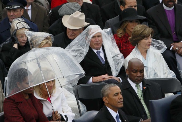 Former president George W. Bush keeps covered in the rain as he sits with his wife Laura at the inauguration ceremonies swearing in Donald Trump as the 45th president of the United States on the West front of the U.S. Capitol in Washington, U.S., January 20, 2017. REUTERS/Rick Wilking