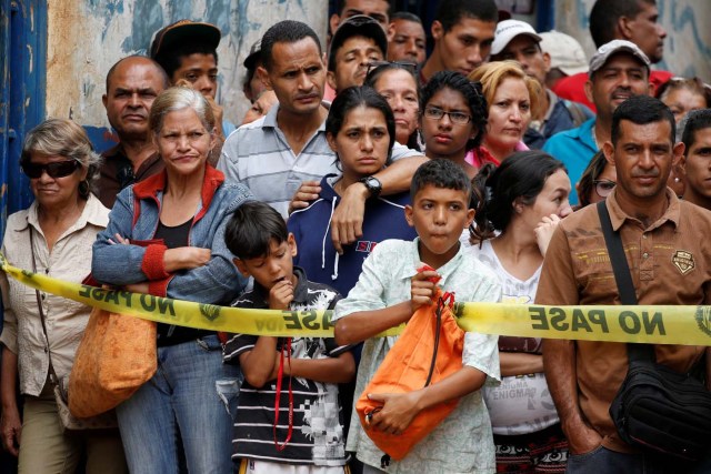 People look at police officers and criminal investigators while they collect evidence in front of a bakery, after it was looted in Caracas, Venezuela April 21, 2017. REUTERS/Carlos Garcia Rawlins TPX IMAGES OF THE DAY