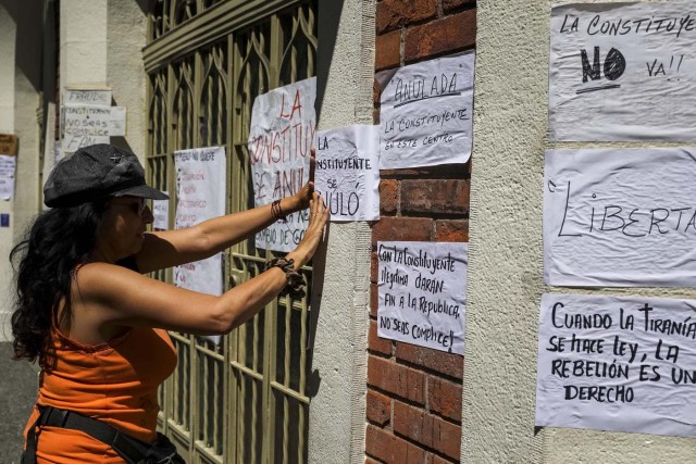 CAR02. CARACAS (VENEZUELA), 24/07/2017.- Una mujer pega carteles en rechazo a la Asamblea Constituyente hoy, lunes 24 de julio de 2017, en una verja de Caracas (Venezuela). Venezuela inicia hoy la semana decisiva para la elección de la Asamblea Nacional Constituyente convocada por el presidente, Nicolás Maduro, con los oficialistas entrando en la recta final de su campaña en medio de protestas y llamados a paro de los opositores en rechazo a esos comicios. EFE/Miguel Gutiérrez