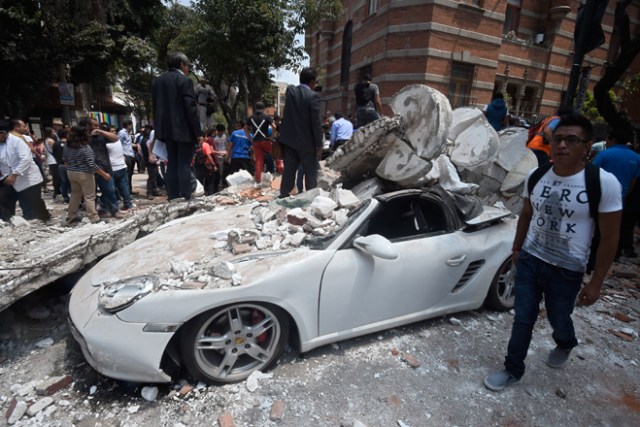 A man stands next to a car crashed by debris from a damaged building after a quake rattled Mexico City on September 19, 2017. A powerful earthquake shook Mexico City on Tuesday, causing panic among the megalopolis' 20 million inhabitants on the 32nd anniversary of a devastating 1985 quake. The US Geological Survey put the quake's magnitude at 7.1 while Mexico's Seismological Institute said it measured 6.8 on its scale. The institute said the quake's epicenter was seven kilometers west of Chiautla de Tapia, in the neighboring state of Puebla. / AFP PHOTO / Alfredo ESTRELLA