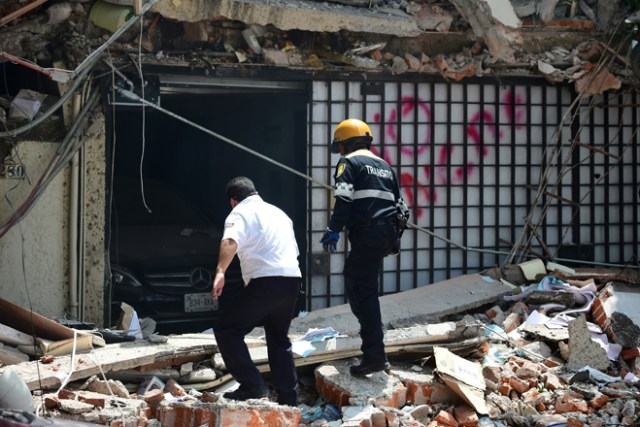 A traffic controller and a security guard look for possible victims at a building which collapsed during a quake in Mexico City on September 19, 2017. A powerful earthquake shook Mexico City on Tuesday, causing panic among the megalopolis' 20 million inhabitants on the 32nd anniversary of a devastating 1985 quake. The US Geological Survey put the quake's magnitude at 7.1 while Mexico's Seismological Institute said it measured 6.8 on its scale. The institute said the quake's epicenter was seven kilometers west of Chiautla de Tapia, in the neighboring state of Puebla. / AFP PHOTO / Ronaldo SCHEMIDT