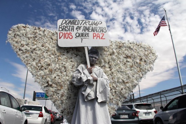 A member of Christian church Salmo 100 dressed as an angel shows a placard addressed to U.S. President Donald Trump that reads "Donald Trump - Enough of Threats - God Wants Peace" in front of the drivers crossing the Cordova-Americas International Bridge between Ciudad Juarez, Chihuahua state and El Paso, Texas on September 23, 2017 in Ciudad Juárez, Chihuahua, Mexico. / AFP PHOTO / HÉRIKA MARTÍNEZ