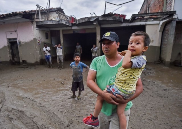 Un hombre sostiene a su hijo en medio de una calle fangosa, después de un alud debido a las fuertes lluvias que afectaron a Corinto en el departamento de Cauca, al suroeste de Colombia el 8 de noviembre de 2017. El deslizamiento de tierra afectó a Corinto el martes por la noche, dejando tres muertos, 32 heridos y 18 desaparecidos, además de cientos de viviendas afectadas, según el último balance proporcionado por las autoridades. / AFP PHOTO / LUIS ROBAYO