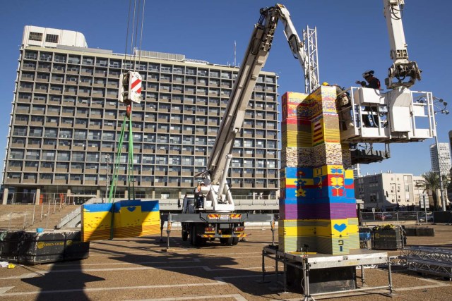 Workers and volunteers help assemble bricks during the construction of a LEGO tower in Tel Aviv's Rabin Square on December 26, 2017, as the city attempts to break Guinness world record of the highest such structure and for it to exceed the height of the municipality building, seen in the background. / AFP PHOTO / JACK GUEZ