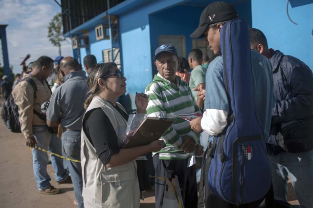 A Brazilian Health Surveillance worker talks with Venezuelans waiting in queue in front of the Brazil Federal Police Office in the border between Venezuela and Brazil at Pacaraima, Roraima, Brazil, on February 28, 2018. According to local authorities, around one thousand refugees are crossing the Brazilian border each day from Venezuela. With the constant influx of Venezuelan immigrants, most are living in shelters and the streets of Boa Vista and Pacaraima cities, looking for work, medical care and food. Most are legalizing their status to stay and live in Brazil. / AFP PHOTO / Mauro Pimentel / TO GO WITH AFP STORY by Paula RAMÓN