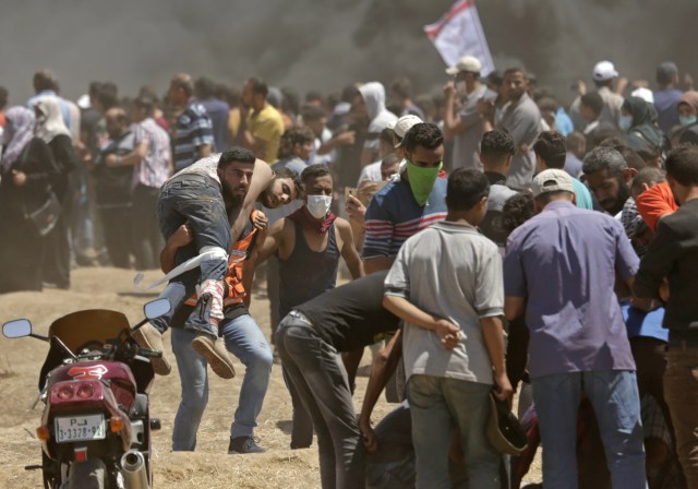 Los palestinos llevan a un manifestante herido durante los enfrentamientos con las fuerzas israelíes cerca de la frontera entre Gaza e Israel al este de la ciudad de Gaza el 14 de mayo de 2018, durante una manifestación el día en que la embajada de EE. UU. Se trasladara a Jerusalén. Estados Unidos traslada su embajada en Israel a Jerusalén el lunes luego de meses de protesta mundial, ira palestina y elogios exuberantes de los israelíes por la decisión del presidente Donald Trump de dejar de lado décadas de precedentes. Existe la preocupación de que las protestas de Gaza a menos de 100 kilómetros (60 millas) de distancia se vuelvan letales si los palestinos intentan dañar o cruzar la valla con francotiradores israelíes posicionados en el otro lado. / AFP PHOTO / MAHMUD HAMS