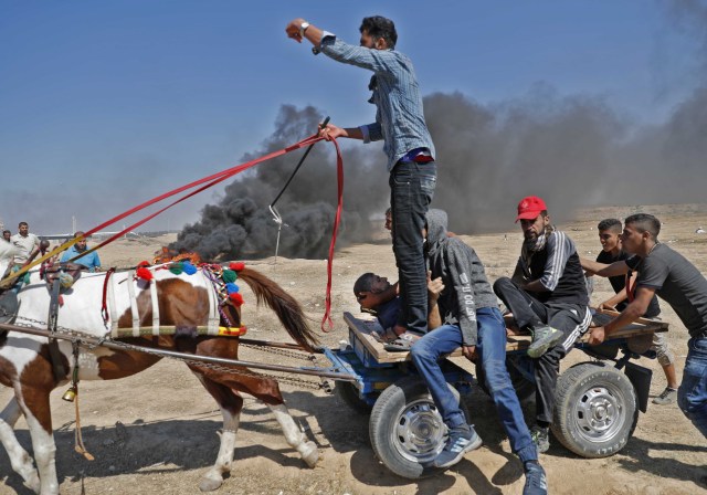 Palestinians transport a demonstrator injured during clashes with Israeli forces near the border between the Gaza Strip and Israel east of Gaza City on May 14, 2018, as Palestinians protest over the inauguration of the US embassy following its controversial move to Jerusalem. Dozens of Palestinians have been killed by Israeli fire on May 14 as tens of thousands protested and clashes erupted along the Gaza border against the US transfer of its embassy to Jerusalem, the Gazan health ministry said. / AFP PHOTO / Thomas COEX