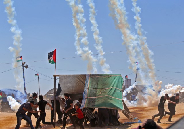 Los palestinos huyen del gas lacrimógeno cerca de la frontera entre Israel y la Franja de Gaza, al este de Jabalia el 14 de mayo de 2018, mientras los palestinos protestan por la inauguración de la embajada de Estados Unidos tras su controvertido traslado a Jerusalén. Decenas de miles de palestinos fueron muertos por disparos israelíes el lunes cuando decenas de miles protestaron y estallaron enfrentamientos a lo largo de la frontera de Gaza contra la transferencia de su embajada a Jerusalén, después de meses de protestas mundiales, ira palestina y elogios exuberantes de los israelíes por la decisión del presidente Donald Trump a un lado décadas de precedente. / AFP PHOTO / Mohammed ABED