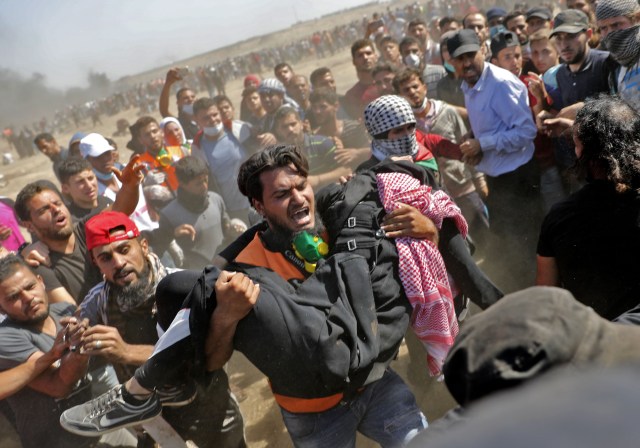 Los palestinos llevan a un manifestante herido durante enfrentamientos con fuerzas israelíes cerca de la frontera entre Gaza e Israel al este de la ciudad de Gaza el 14 de mayo de 2018, mientras los palestinos protestan por la inauguración de la embajada de Estados Unidos tras su controvertido traslado a Jerusalén. Docenas de palestinos fueron asesinados por disparos israelíes el 14 de mayo cuando decenas de miles protestaron y estallaron enfrentamientos a lo largo de la frontera de Gaza contra la transferencia de su embajada a Jerusalén, luego de meses de protestas globales, ira palestina y elogios exuberantes de los israelíes por el presidente Donald Trump decisión dejando de lado décadas de precedentes. / AFP PHOTO / Thomas COEX